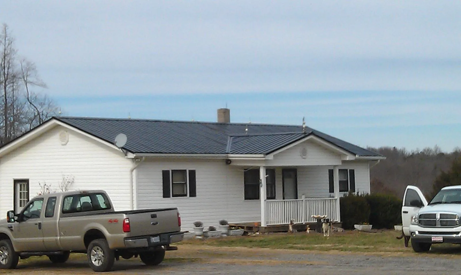 Finished dark metal roof on a white ranch home with work trucks parked in Centerville